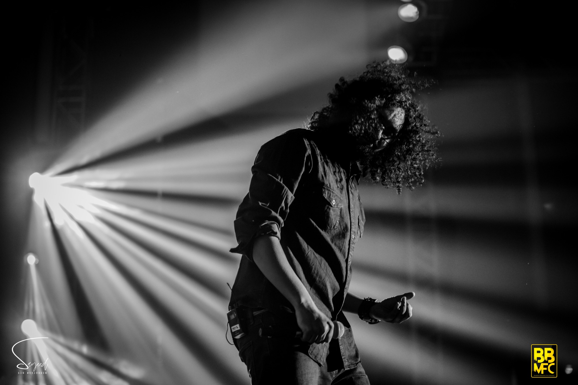 Silhouette of a curly-haired performer caught in a burst of stage light rays, black-and-white, Shironamhin concert in Dhaka — Sayeed BM