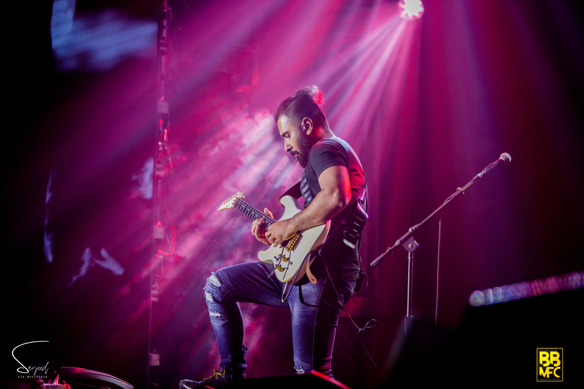 Guitarist seated with a white Stratocaster under pink and purple light rays at a Shironamhin concert in Dhaka — Sayeed BM