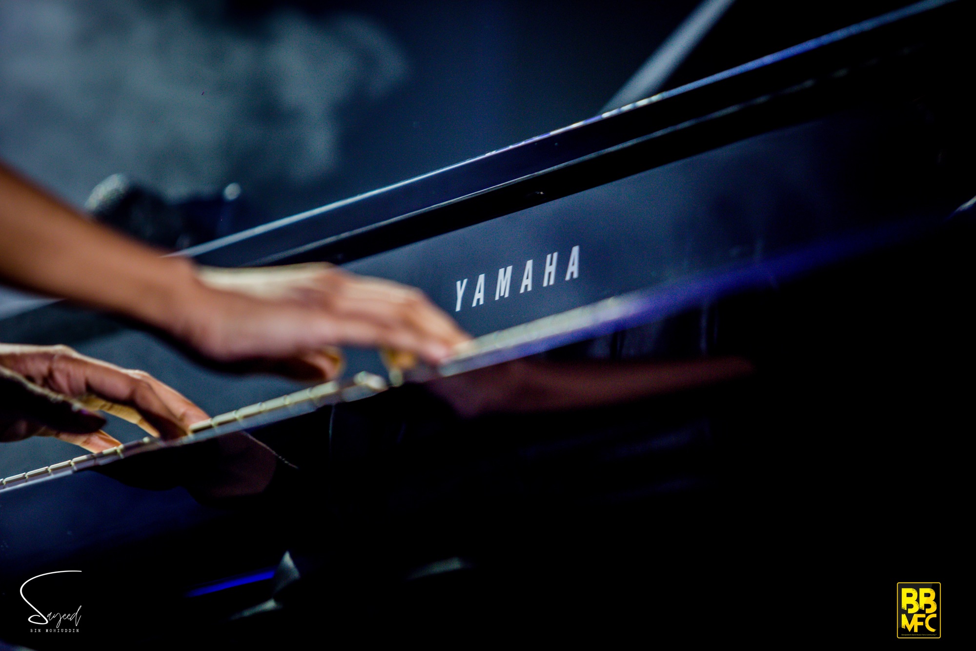 Close-up of a pianist's hands resting on piano keys with YAMAHA branding visible, black-and-white, Shironamhin concert in Dhaka — Sayeed BM