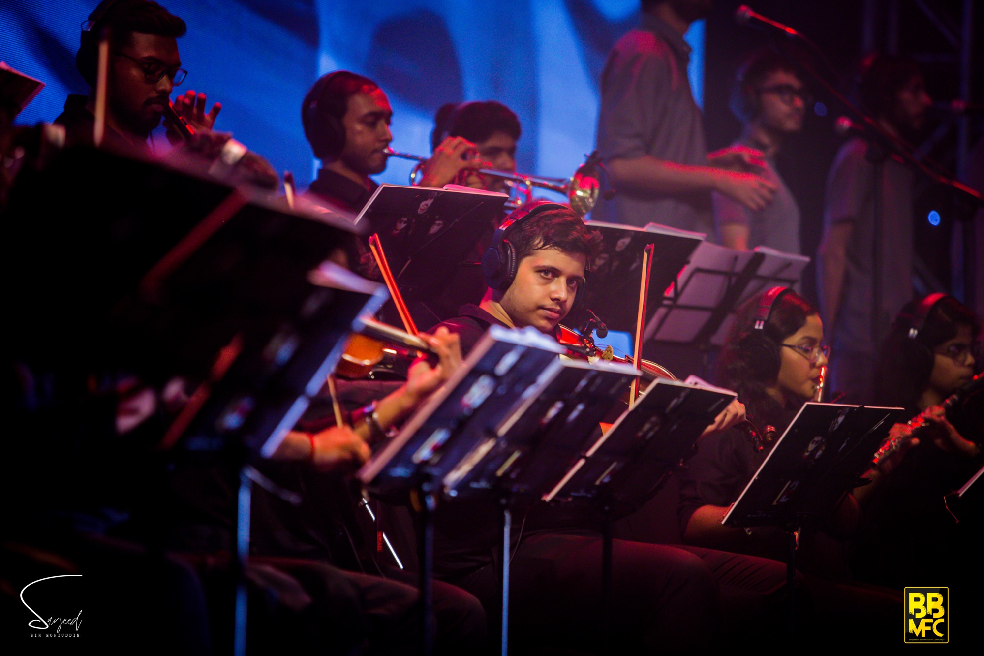 String section musicians with headphones performing together under blue and red light at a Shironamhin concert in Dhaka — Sayeed BM