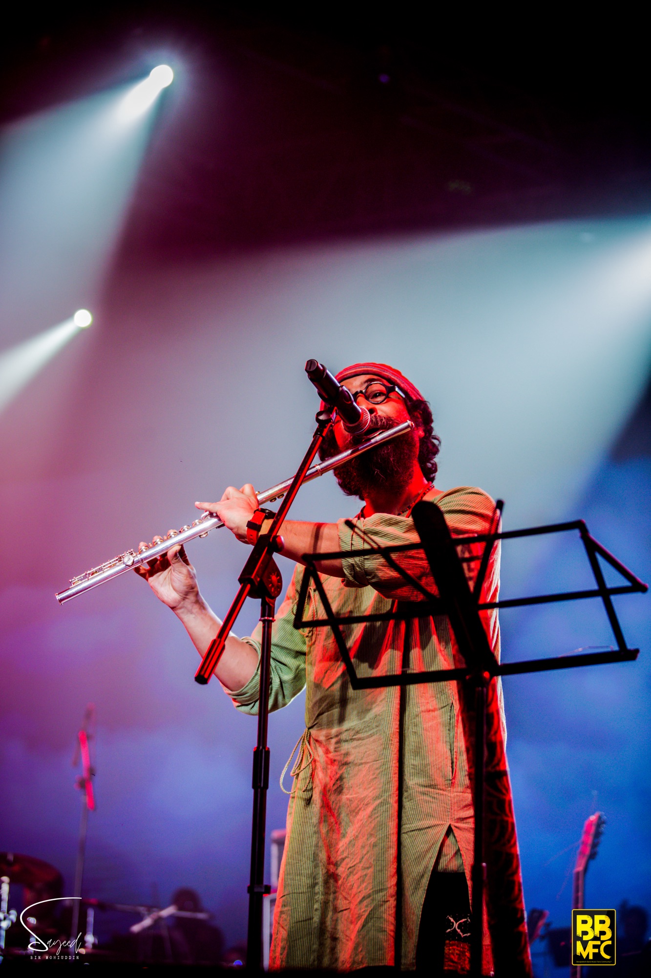Flute player in a red headwrap performing under red and blue light rays at a Shironamhin concert in Dhaka — Sayeed BM
